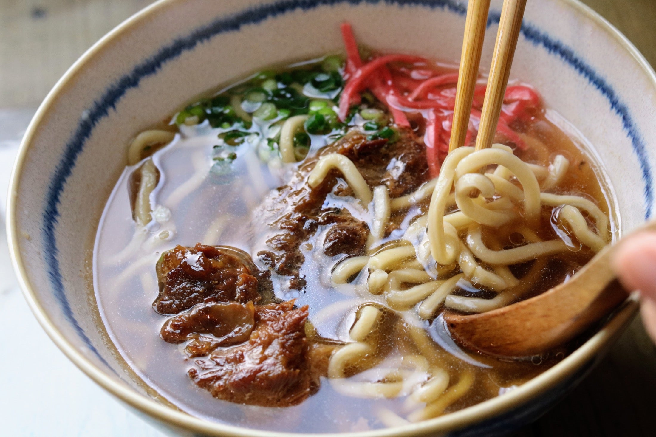 店で提供する沖縄そばから箸で麺を持ち上げる様子